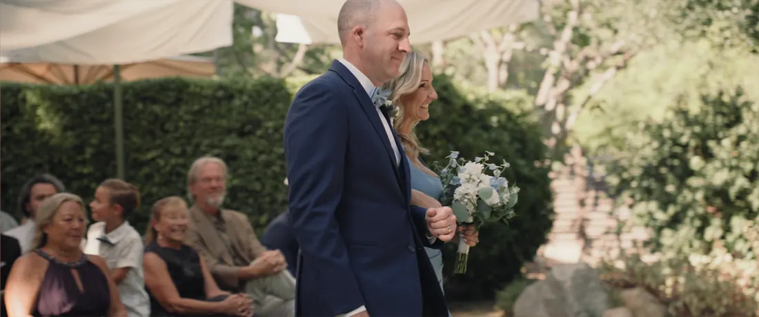 A father walks the bride down the aisle between tall hedges at Maravilla Gardens